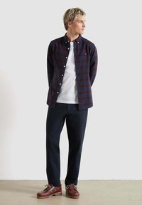 Camicia a quadri blu e rossi sopra una t-shirt bianca, abbinata a pantaloni scuri e scarpe marroni con lacci e suole testurizzate.