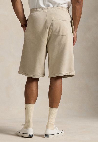 Beige bomullsshorts med elastisk midje, sidelommer og en baklomme. Brukt med hvite sneakers og kremfargede sokker.