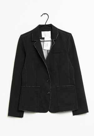 Schwarzer maßgeschneiderter Blazer mit zwei Fronttaschen und kontrastierenden weißen Nähten, hängend an einem schwarzen Kleiderbügel vor weißem Hintergrund.