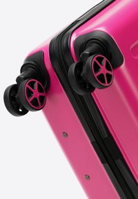 Valigia rigida rosa con zip nera e ruote accentate caratterizzate da un design a razze. Texture liscia, design compatto e materiale durevole.