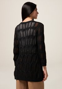 Cardigan nero lavorato a maglia con un design ad intreccio di modelli geometrici, maniche lunghe e vestibilità comoda, che arriva a metà coscia.