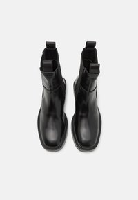 Black leather ankle boots with elastic side panels, flat soles, and pull tabs at the back for easy wear. Smooth texture and minimal design.