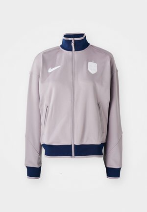 Light gray athletic jacket with a high collar, zip closure, navy accents, two side pockets, and a logo detail on the chest.