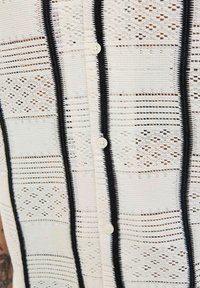 Chemise à boutons en dentelle blanche avec des rayures verticales noires. Présente des motifs complexes, une texture légère et des boutons ronds.