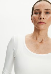 Biała bluzka z długim rękawem i okrągłym dekoltem, wykonana z prążkowanej tkaniny. Posiada dopasowany fason, podkreślający kształt tułowia.