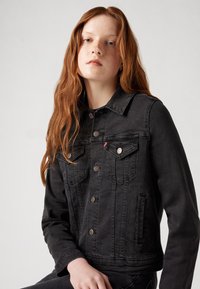 Giacca in denim nera con design classico, chiusura frontale con bottoni, due tasche sul petto e una leggera texture.