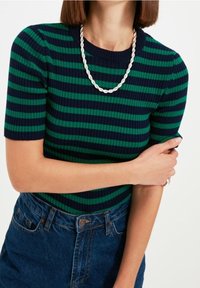 Haut en maille côtelée à rayures dans des tons bleu marine et vert, col rond, manches courtes, associé à une jupe en denim, présentant un motif texturé.