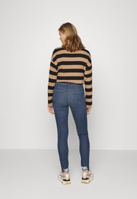 Top de mangas longas listrado em preto e bege, emparelhado com jeans skinny azul escuro. Ténis têm um design bege e preto com solas brancas.