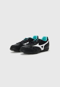 Botas de fútbol negras con una superficie texturizada y acentos blancos. Cuenta con una lengüeta acolchada, forro turquesa y suela de goma negra.