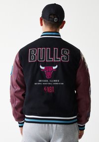 Fekete és bordó egyetemi dzseki "BULLS" logóval, Chicago címerrel, domború bika fejjel, kék és fehér csíkos bordás mandzsettákkal és aljjal.
