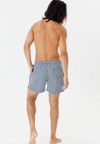Gestreifte Badeshorts in Marineblau und Weiß, mit einem Kordelzug-Bund, zwei Seitentaschen und einer hinteren Tasche mit Klappe.