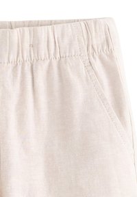 Pantaloni beige chiaro in tessuto testurizzato, con cintura elastica e tasche laterali. Il tessuto appare morbido e traspirante, adatto per un abbigliamento casual.