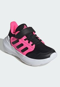 Black and pink athletic shoe with a mesh upper, Velcro strap, black accents, and a white rubber sole. Features three stripes design.