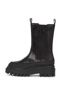 Botas negras hasta el tobillo con una suela de goma gruesa, que presentan un exterior de cuero suave, paneles laterales elásticos y bucles de arrastre para facilitar su colocación.