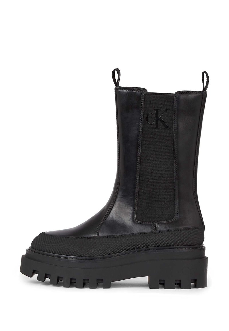 Botas negras hasta el tobillo con una suela de goma gruesa, que presentan un exterior de cuero suave, paneles laterales elásticos y bucles de arrastre para facilitar su colocación.