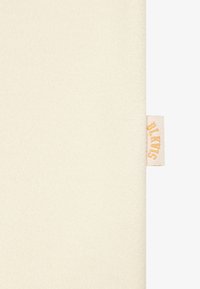 Coperta in pile color crema con una texture morbida. Presenta un piccolo etichetta di tessuto con la scritta "BLANK" in lettere arancioni sul bordo.
