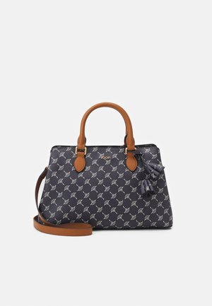 Sac à main noir avec motif géométrique blanc, poignées marron et bandoulière marron détachable, avec un petit nœud décoratif sur le côté.