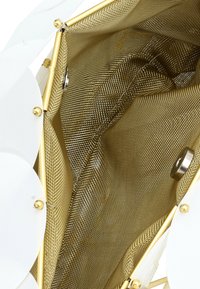 Interiér bílé kabelky s zlatou síťovinou. Design zahrnuje strukturovaný tvar se zlatým kováním a hladkými texturami.