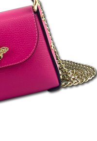 Roze leren handtas met een gouden kettingriem, met een klep sluitsysteem en een vlinderaccent aan de voorkant. Gladde textuur en gestructureerde vorm.