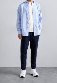 Camicia a quadri azzurro chiaro button-up sopra una T-shirt crema, abbinata a pantaloni sportivi blu navy e sneakers bianche.