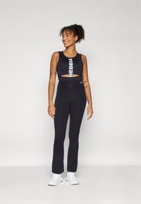 Black athletic set featuring a cropped tank top with cutout design and white logo, paired with high-waisted, fitted leggings.