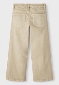 Beige farkut, joissa on leveä lahja ja korkea vyötärö, takana paikka-taskut ja hienovarainen rakenne. Siistit linjat ilman merkittäviä koristeita.