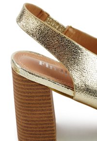 Gouden metalen sleehak sandaal met een gestructureerde afwerking. Heeft een brede slingbackband en een vierkante houten blokhak met horizontale groeven.