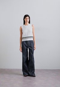 Top senza maniche a maglia grigia con una striscia contrastante bianca e nera in vita, abbinato a pantaloni a gamba larga in denim scuro a vita alta.