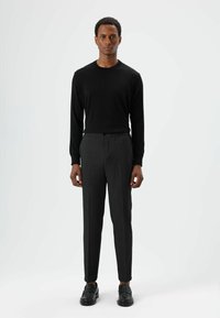 Zwarte trui met lange mouwen gecombineerd met donkergrijze, op maat gemaakte broek. De broek heeft een knoop en elastische tailleband, een gladde textuur en een recht model.