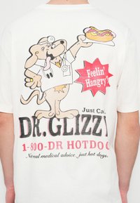 Hvit t-skjorte med tegneseriehund iført legefrakk, som holder en pølse i brød. Teksten inkluderer "DR. GLIZZY" og "Feelin' Hangry?" i sterke farger.