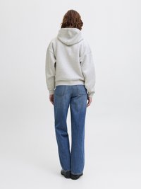 Sweatshirt cinza com capuz, mangas largas e um corte descontraído, combinado com umas calças de ganga azuis de corte reto e costuras visíveis.