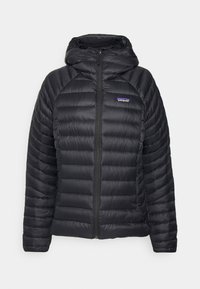 Zwarte pufferjack met een ritssluiting en capuchon. Heeft een gewatteerd patroon en een logo-label op de linkerborst. Soepele, lichte stof.