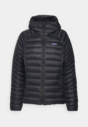 Zwarte pufferjack met een ritssluiting en capuchon. Heeft een gewatteerd patroon en een logo-label op de linkerborst. Soepele, lichte stof.