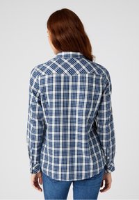 Camicia a maniche lunghe a quadretti in blu navy e bianco, con colletto button-down, yoke dritto sul retro e orlo arrotondato. Tessuto in cotone con una texture liscia.