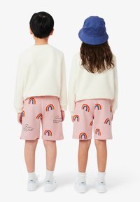Pantalones cortos rosas con estampados de arcoíris, fabricados en algodón, con una cintura elástica. Combinados con suéteres blancos y zapatillas, un sombrero de cubo azul llevado por uno de ellos.