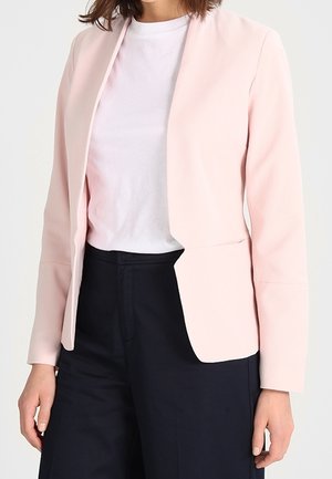 Blazer rose pâle en tissu lisse avec un design minimal, présentant des manches longues, une ouverture à l'avant et deux poches avant. Associé à une chemise blanche.