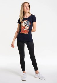 Musta t-paita, jossa on "Tom ja Jerry" -grafiikka; lyhyet hihat, pyöreä kaula-aukko, puuvillasekoitetta. Yhdistetty mustien skinny-farkkujen ja valkoisten tennarien kanssa.
