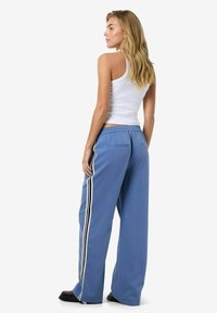 Pantalons larges bleu clair avec des rayures latérales noir et blanc, dotés d'une taille élastique à cordon de serrage et de poches arrière. Tissu lisse et léger.