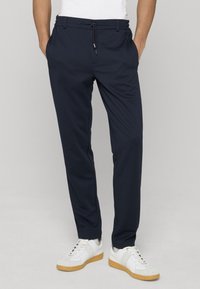 Jogging bleu marine avec une taille à cordon, poches latérales et jambes fuselées, assorti à des baskets blanches avec une semelle en caoutchouc.