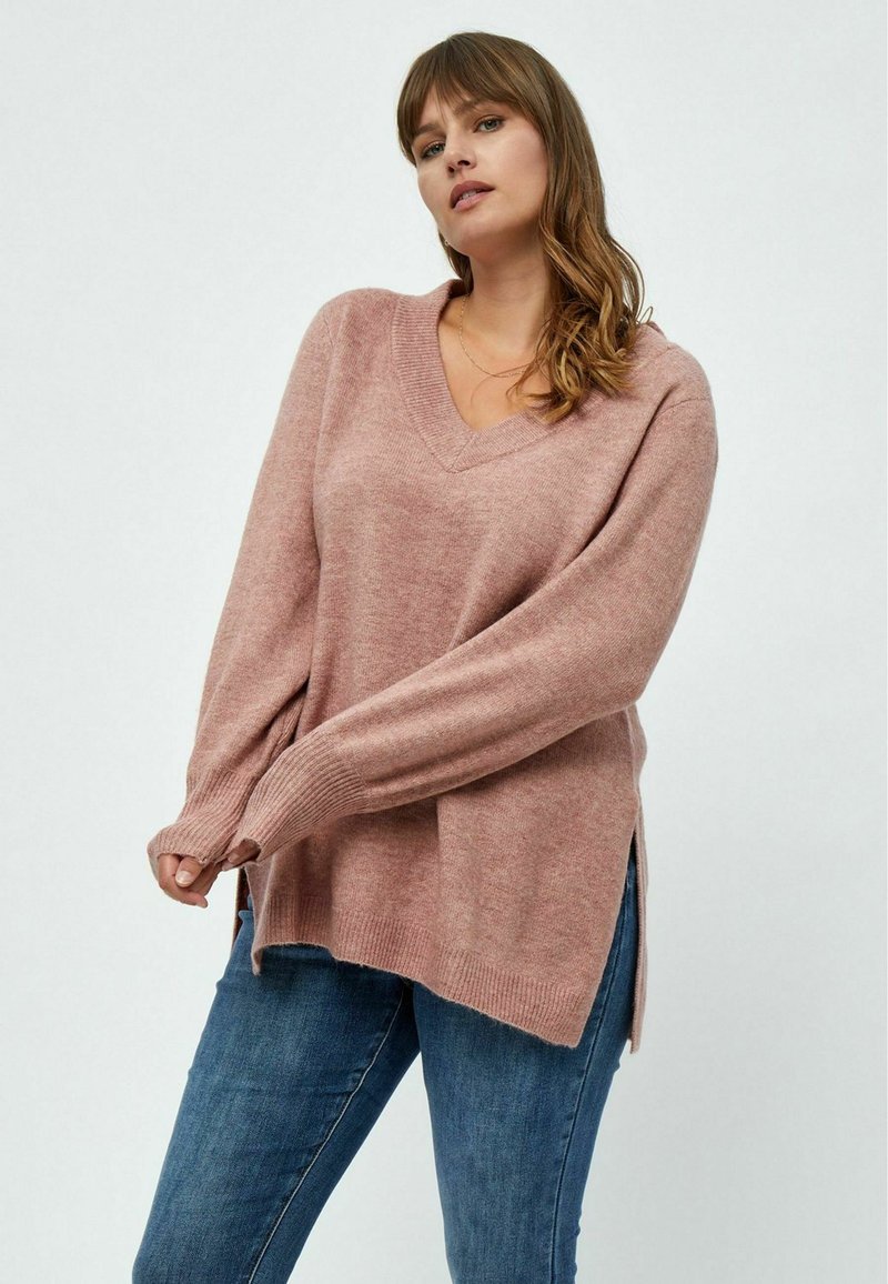 V-Ausschnitt, langärmliger Pullover aus weichem, rosa Strick mit gerippten Bündchen und seitlichen Schlitzen. Kombiniert mit hellblauen Jeans hat er eine lockere Passform und Textur.