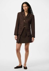 Blazer marron avec un bouton en or, associé à une mini jupe assortie. Tissu lisse, design structuré, comprenant des poches latérales et une fente.