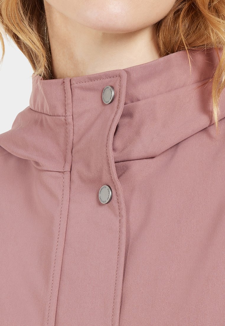 Hellrosa Jacke mit hohem Kragen, aus glattem Material und mit zwei metallischen Druckknöpfen, die ein minimalistisches Design betonen.