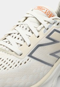 Baskets de course blanches avec tige en mesh, panneau texturé, accents gris clair et étiquette de marque réfléchissante. Comprend des lacets plats et un design perforé.