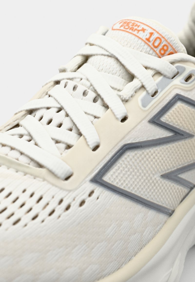 Baskets de course blanches avec tige en mesh, panneau texturé, accents gris clair et étiquette de marque réfléchissante. Comprend des lacets plats et un design perforé.