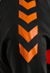 Sort stof med fem stablede orange nedadgående Chevron-striber trykt lodret.