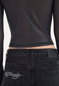 Black denim jeans feature a high waist, back pocket embroidery, and a textured, smooth black textile with a leather patch at the waist.