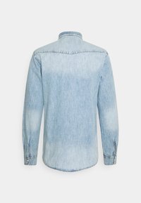 Hellblaues Denim-Hemd mit langen Ärmeln und knöpfbaren Manschetten, sichtbaren Nahtnähten und Kragen, von hinten auf einem weißen Hintergrund gezeigt.