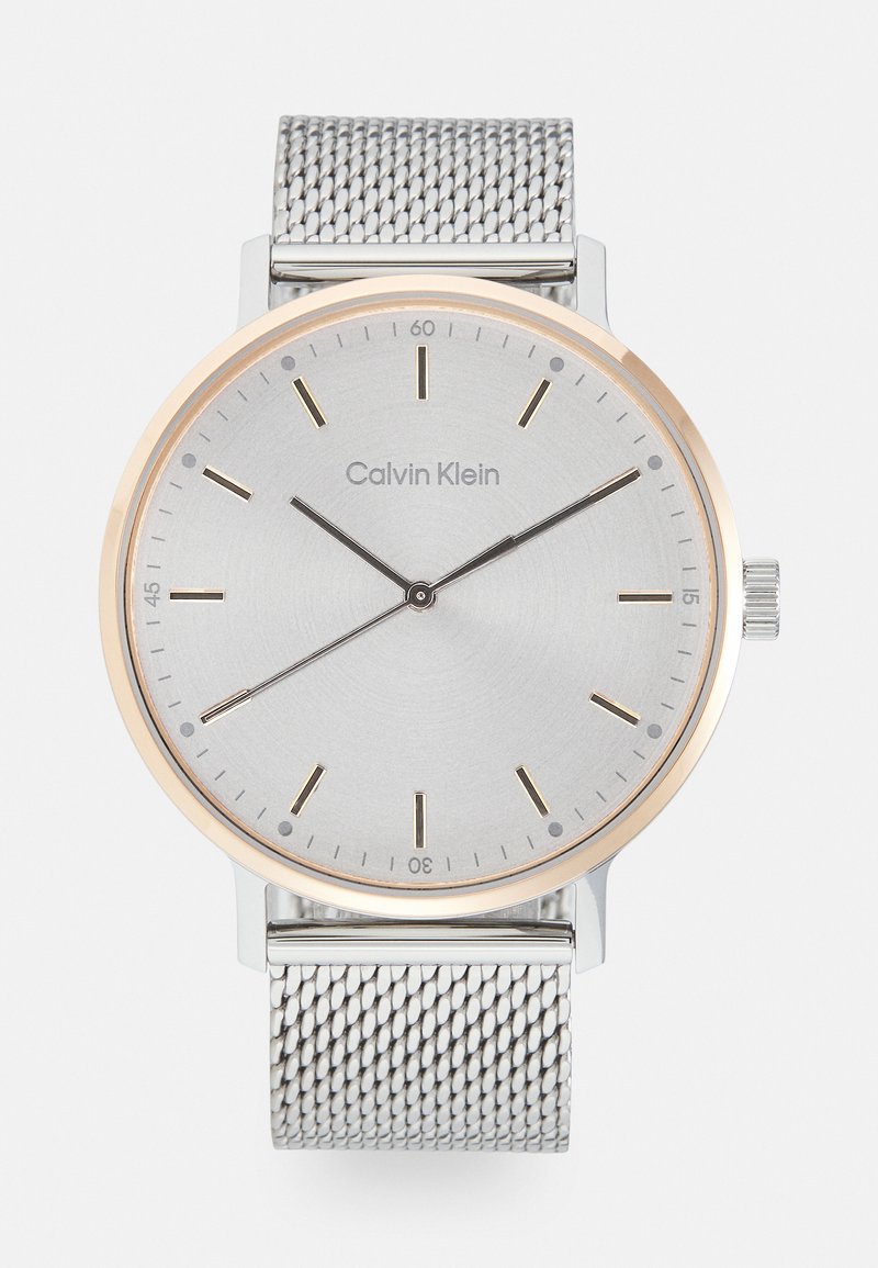 Silberne Analog-Uhr mit einem gebürsteten silbernen Zifferblatt und einer goldfarbenen Lünette. Sie verfügt über goldfarbene Stundenmarkierungen, schwarze Zeiger und ein silbernes Mesh-Armband.