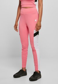 Rosa leggings med hvite og svarte sidepaneler, høy midje, glatt stoff og tettsittende design. Logo synlig på låret.