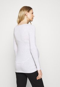 Camisa de maternidade de mangas longas cinza, feita de tecido leve, com uma bainha curva e um corte relaxado para conforto na região da barriga.